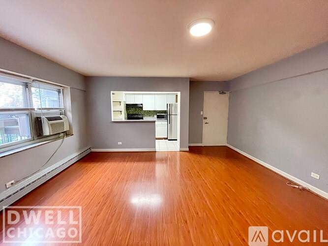 A spacious room with wooden flooring and a large window on the left side.