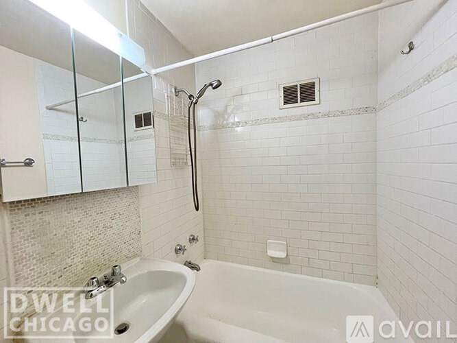 A white tiled bathroom with a white bathtub and a white sink.