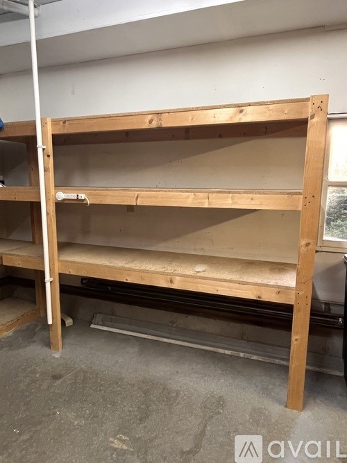 A wooden shelving unit with three shelves is in a room with a white ceiling and a window.