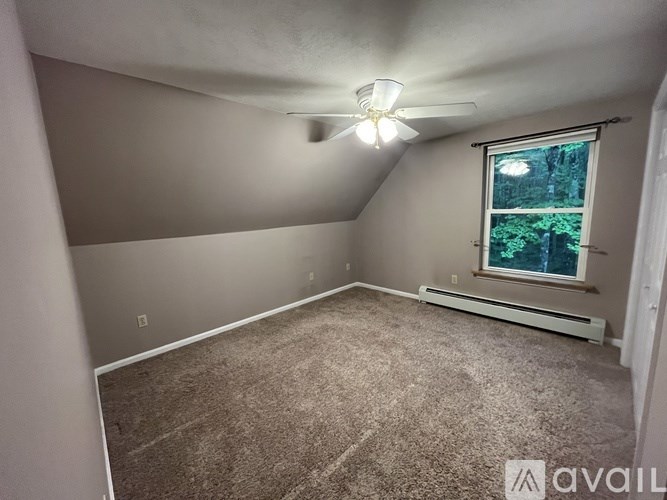 A room with a ceiling fan and a window with a view of trees.
