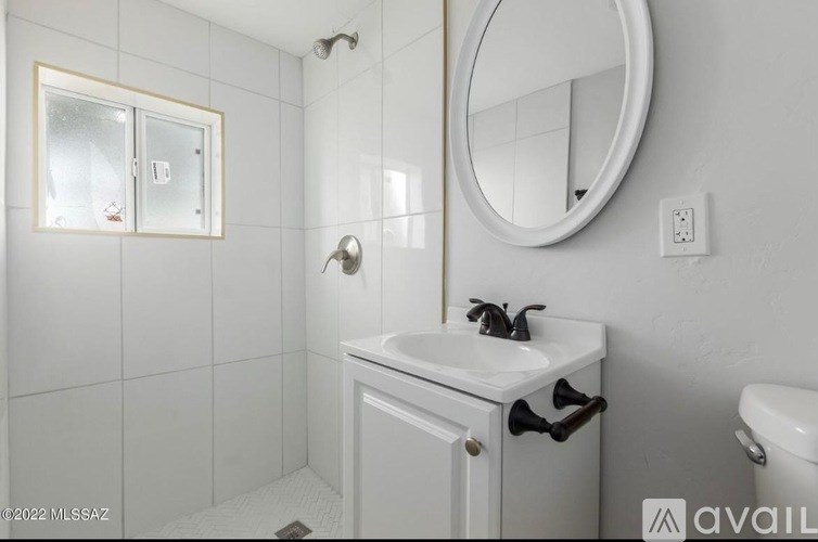 A white bathroom with a round mirror and a white sink.