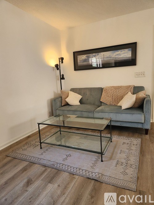 A grey couch with a glass coffee table in front of it.