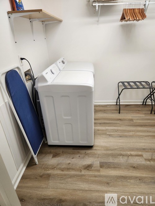 A white washing machine is in a laundry room with a blue chair and a black and white striped stool.