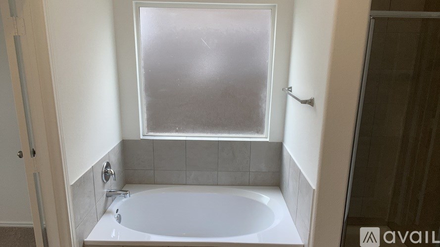 A white bathtub is in a bathroom with a window above it.