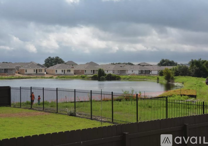 A person is standing on a path near a lake in a residential area.