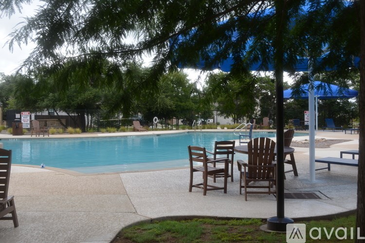 A pool surrounded by chairs and trees.