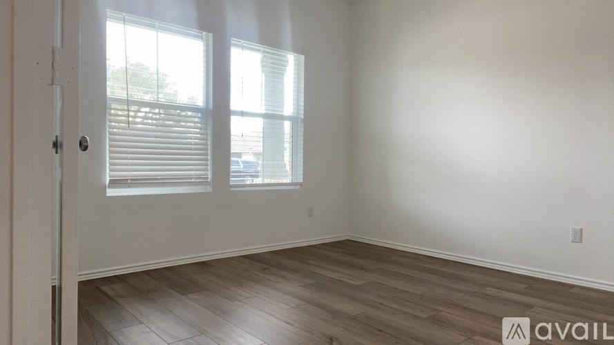 A room with wooden flooring and two windows with blinds.