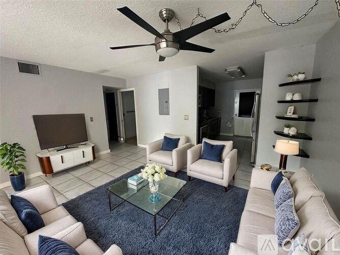 A living room with a ceiling fan and a glass coffee table.