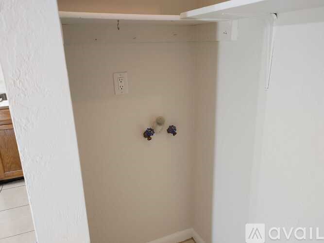 A small white room with a wall outlet and a small shelf above it.