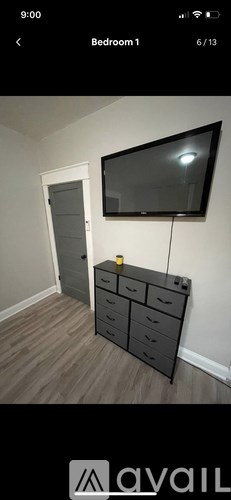 A black dresser with a flat screen TV mounted above it in a room with wooden flooring.