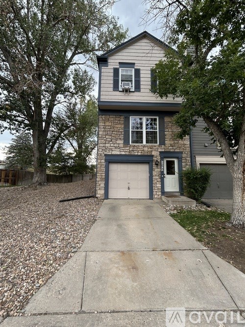 A two-story house with a garage is surrounded by trees and has a driveway leading to the front door.