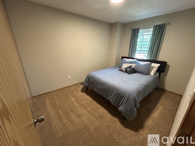 A bedroom with a bed, carpet, and a window with green curtains.