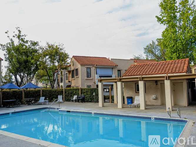 A swimming pool in front of a house with a blue umbrella and white chairs.