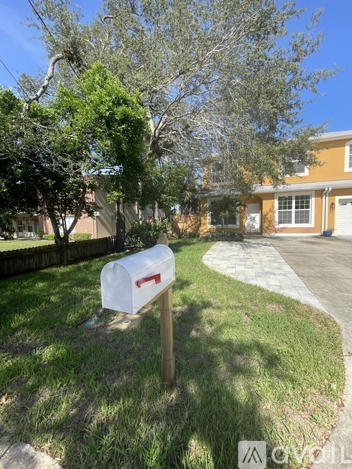 A white mailbox stands on a grassy lawn in front of a yellow house.