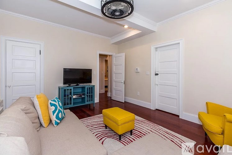 A living room with a yellow ottoman and a white couch.