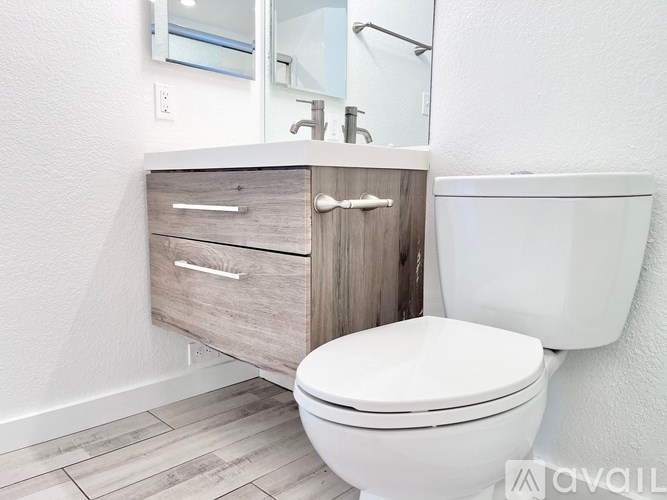 A white toilet sits next to a white sink with a wooden cabinet.