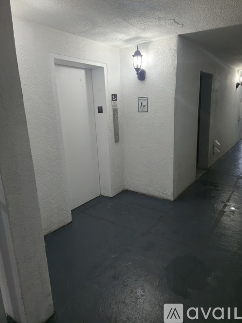 A hallway with a light on the wall and a door on the left.