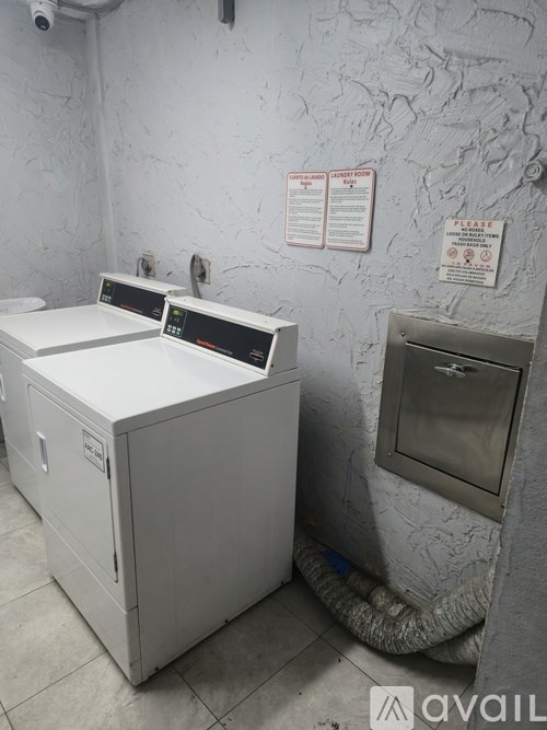 A white industrial washing machine sits in a room with a wall covered in scratches and scuffs.