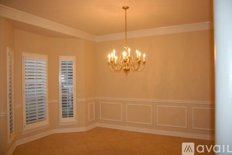 A room with a chandelier, two windows with shutters, and a wall with a panel design.