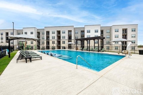 A swimming pool is surrounded by lounge chairs in front of apartment buildings.
