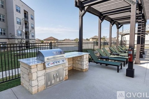 A BBQ grill is on a stone block and there are green chairs around it.