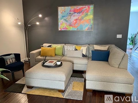 A living room with a grey couch, a small ottoman, and a painting on the wall.