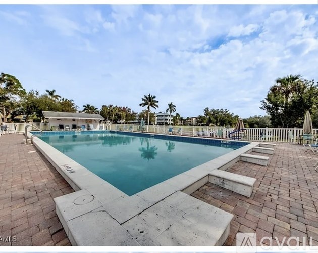 A large outdoor swimming pool surrounded by a brick patio and palm trees.