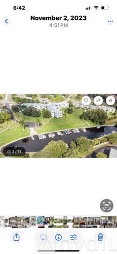 A screenshot of a phone showing a park with a parking lot and a building in the background.