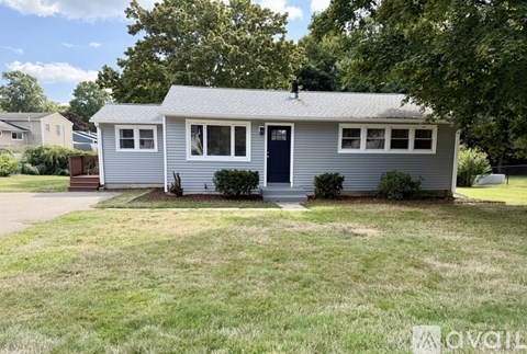 A small house with a grey roof and a black door is surrounded by a well-kept lawn.
