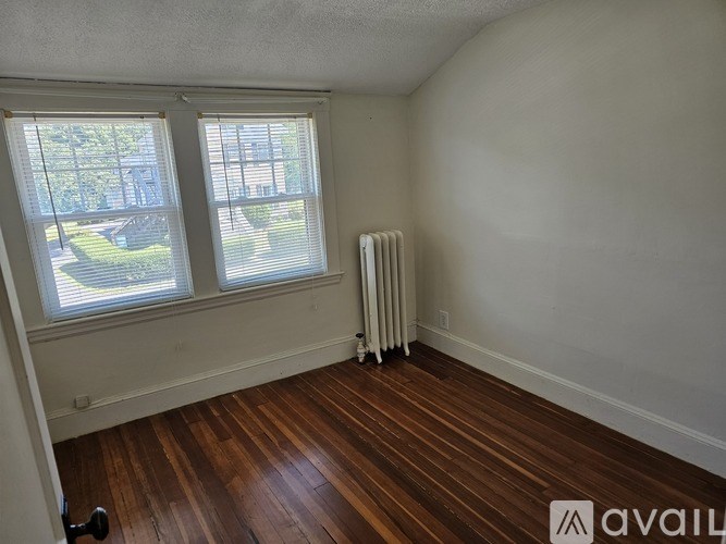 A room with a wooden floor and a window with a view of a tree-lined street.