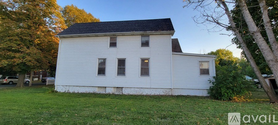 A white house with a black roof and a sign that says "available" in the front yard.