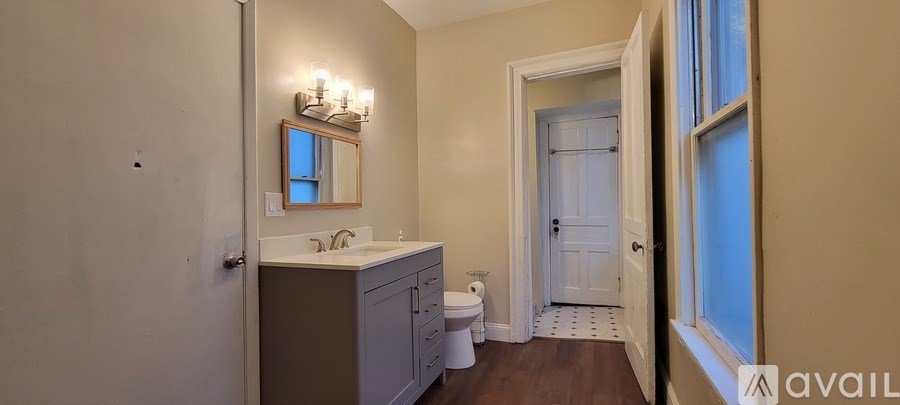 A bathroom with a toilet, sink, mirror and a window.