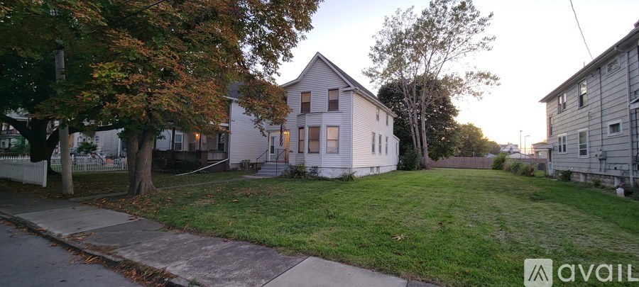 A house with a white fence and a tree with orange leaves in front of it.