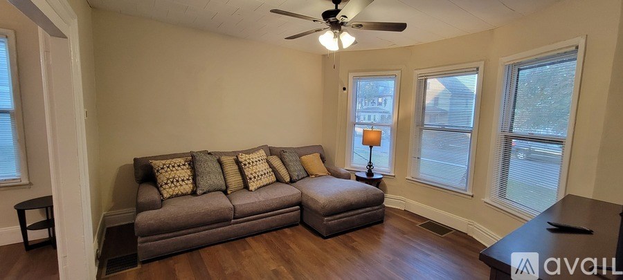 A living room with a grey couch and a fan on the ceiling.