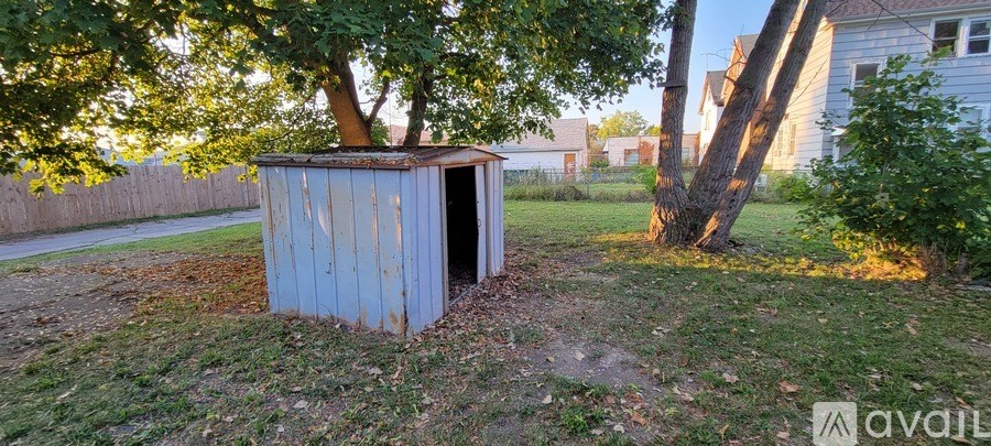 A blue shed sits in a grassy area next to a tree.