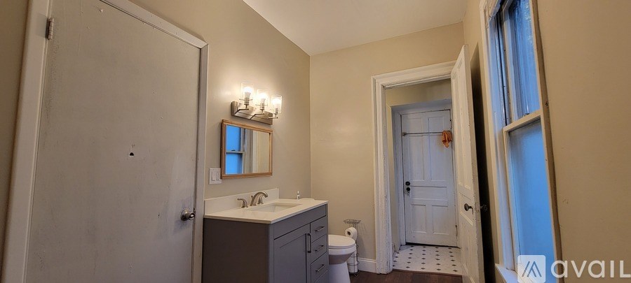 A bathroom with a toilet, sink, mirror and a window.