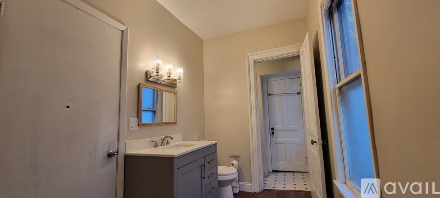 A bathroom with a mirror, sink, toilet and a window.