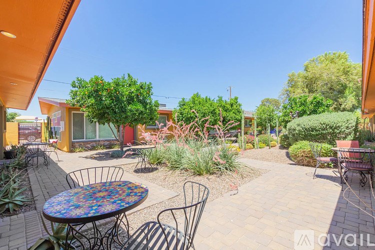 A patio with a table and chairs is surrounded by plants and trees.
