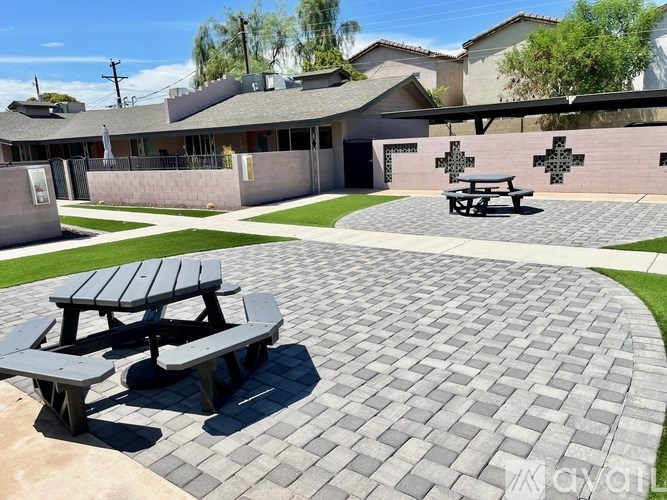 A picnic table sits on a brick patio in front of a building with a cross painted on the wall.