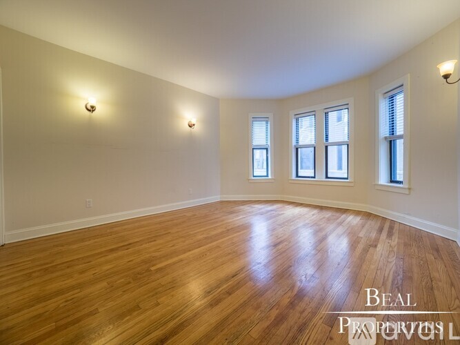 A room with wooden floors and three windows.