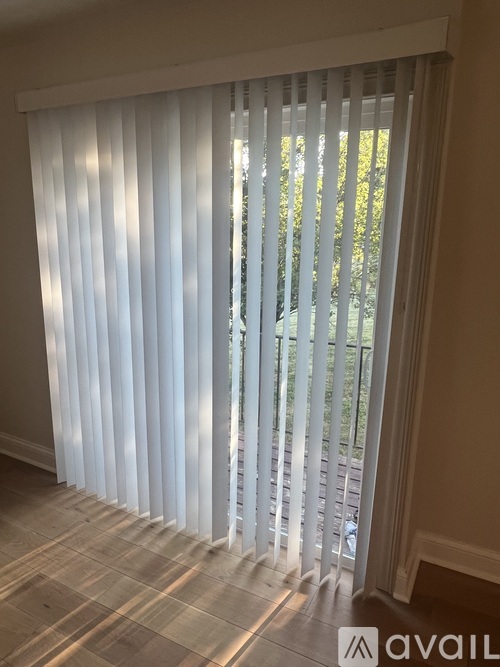A white blind is open to a view of trees outside.