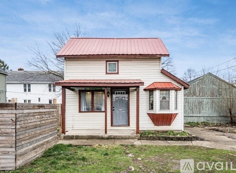 A small house with a red roof and a wooden fence in front.