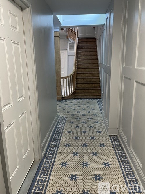 A hallway with a tiled floor and a staircase in the background.