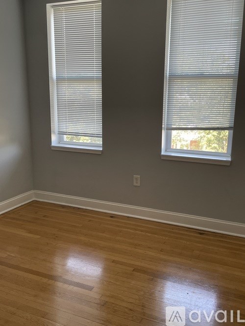 A room with wooden floors and two windows with blinds.