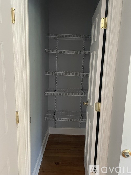 A white door with a gold handle is open to a white hallway with a white door on the other side.