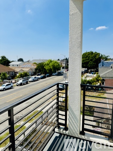 A balcony with a metal railing overlooks a street with cars and houses.