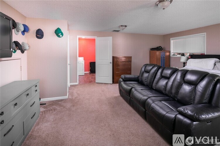 A black leather couch sits in a living room with a grey dresser and a television.