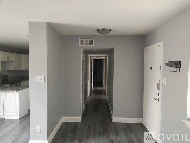 A hallway with a door on the right and a kitchen area on the left.