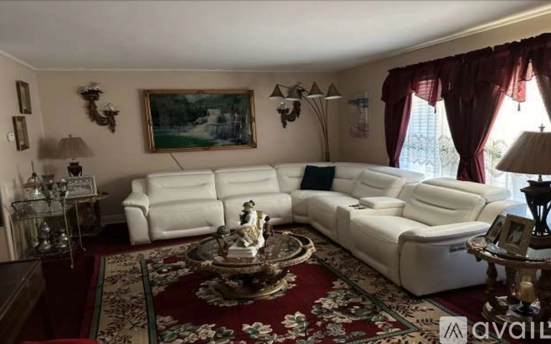 A living room with white furniture and a painting on the wall.