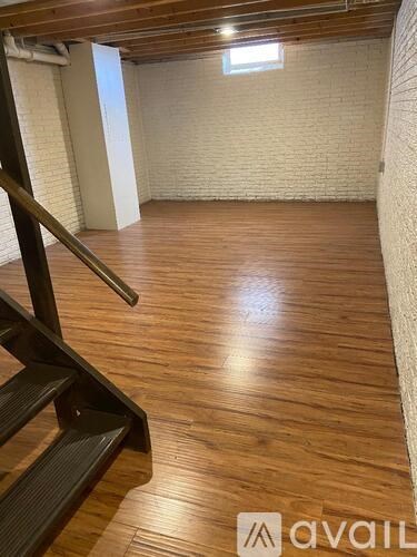 A room with wooden flooring and a staircase on the left side.